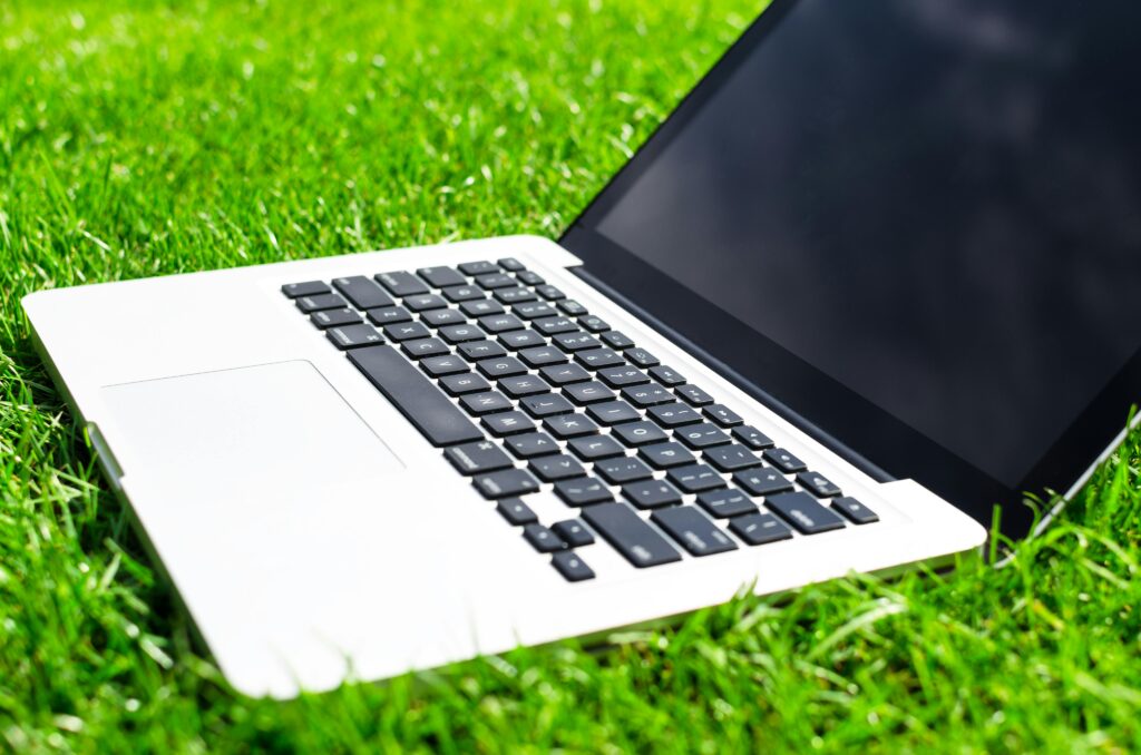 A modern open laptop with a black screen placed on lush green grass, symbolizing technology and nature.
